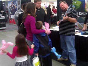 Photo of parents speaking with exhibitor while children play with their balloon animals