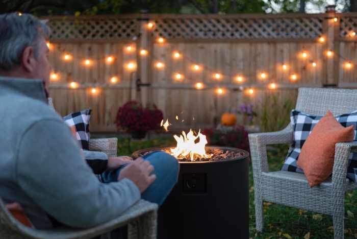 Photo of a man seated around a firepit with lights in a small courtyard garden.